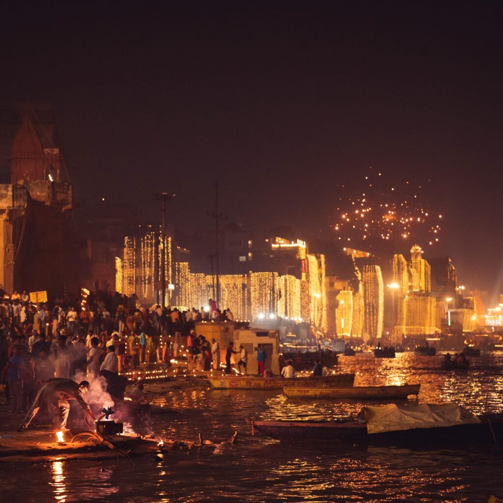 Dusk on the Ganges River, Varanasi, with a festive crowd and illuminated buildings during a traditional ceremony.